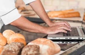 Nahaufnahme der Hand des männlichen Bäckers unter Verwendung des Laptops cloud lösung rezepten online shop echtzeit analysen personalverwaltung kosten administration optimierung